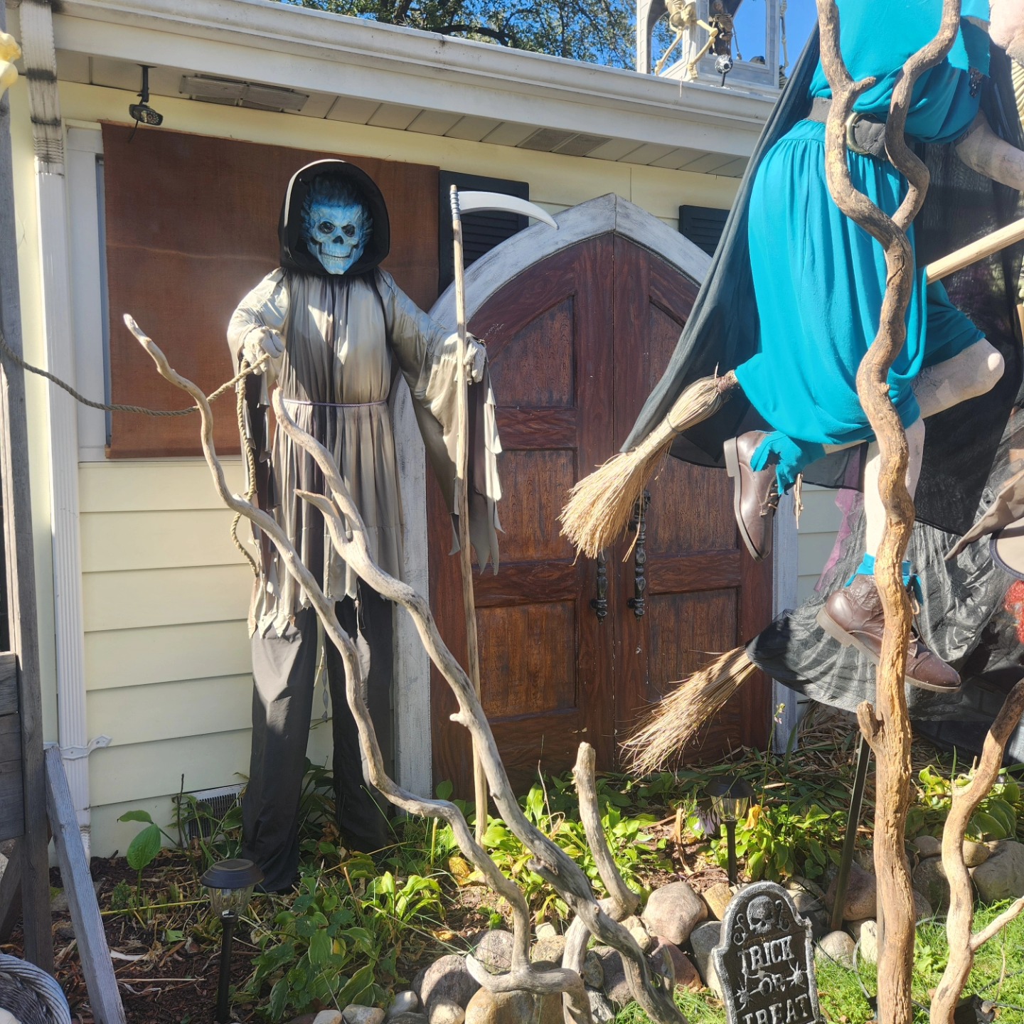 A hooded blue-faced reaper beside a cemetery arch and crooked branches — Hills of Unrest, October 2024.