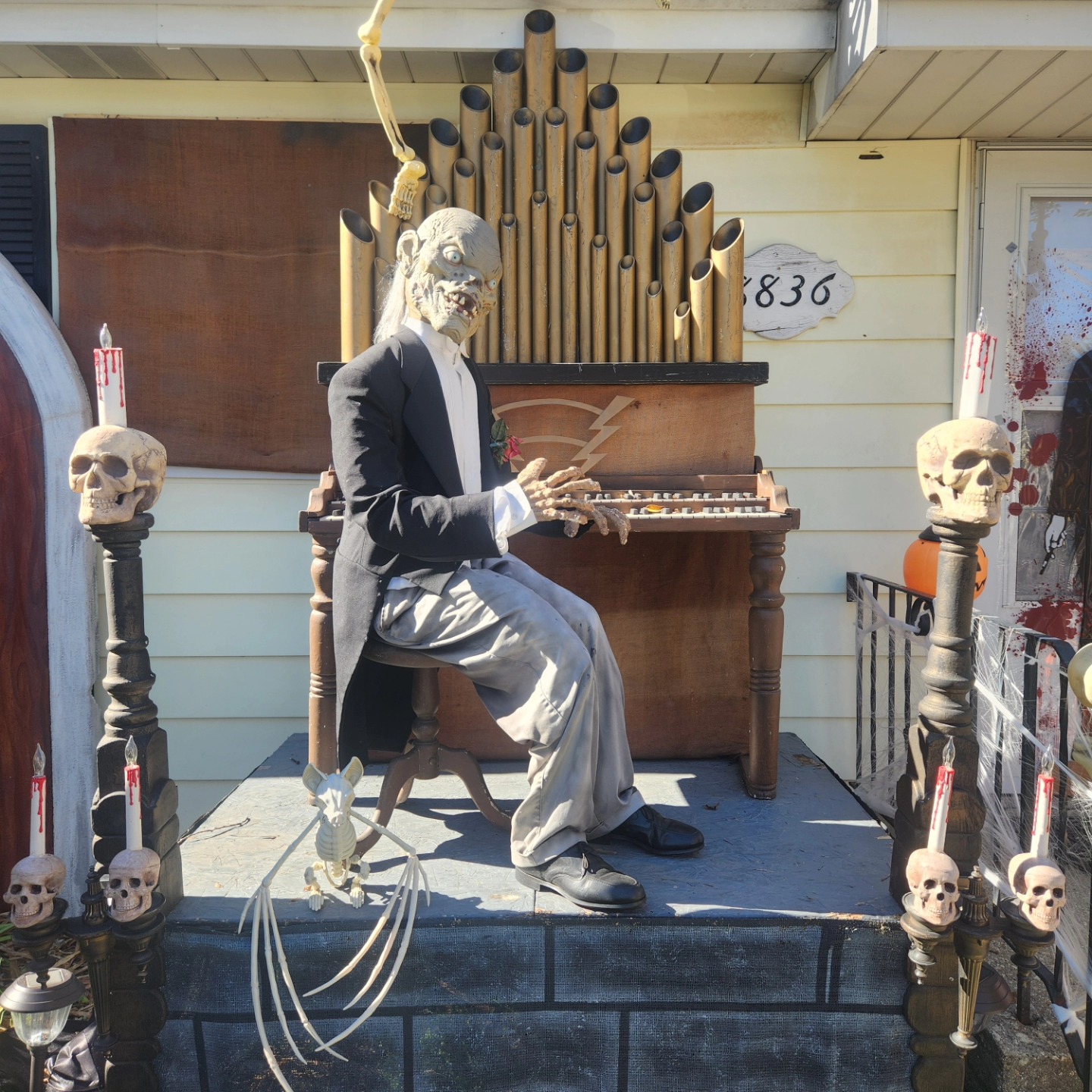 An elderly horror figure seated at an upright organ, surrounded by skull-topped posts — Hills of Unrest, October 2024.