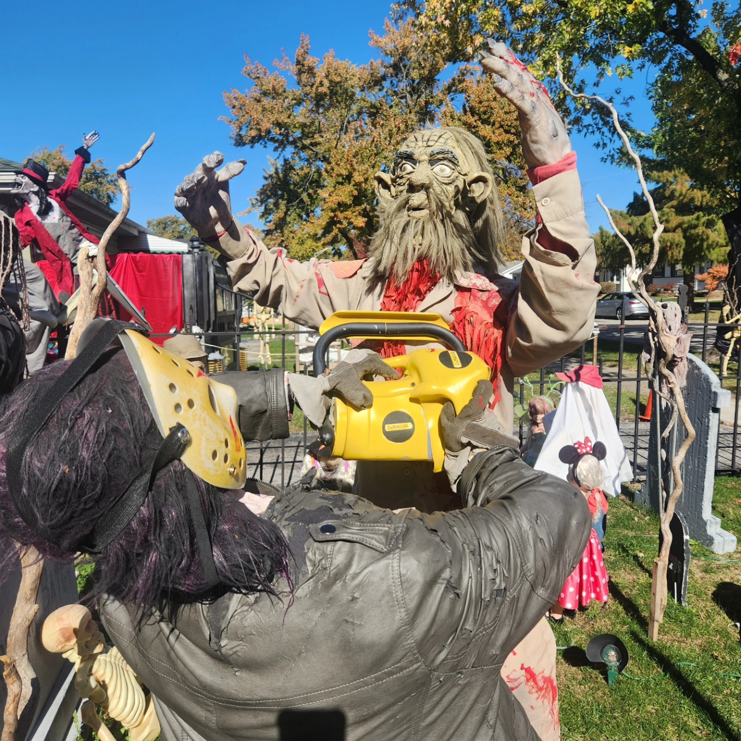 Close view of a horror figure with a prop yellow chainsaw among the cemetery figures — Hills of Unrest, October 2024.